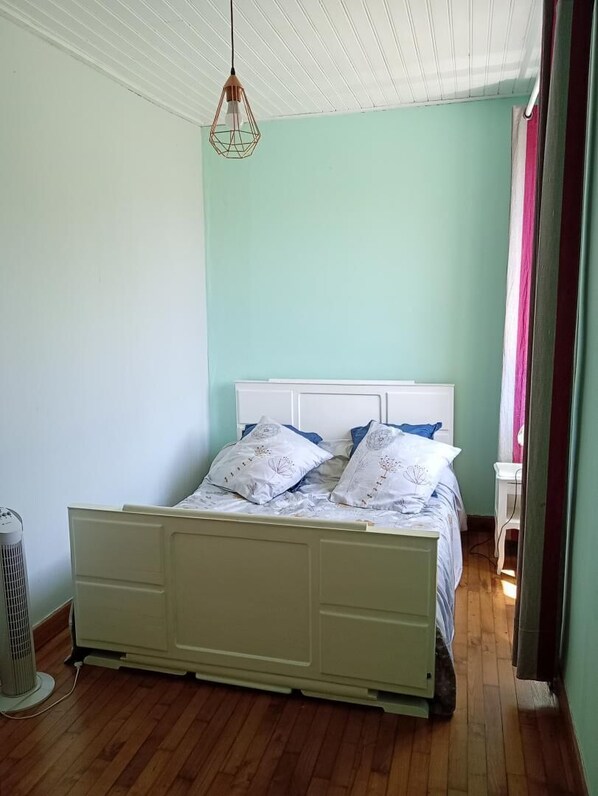A bedroom with a bed, a bedside table, a hanging light fixture, and a radiator.