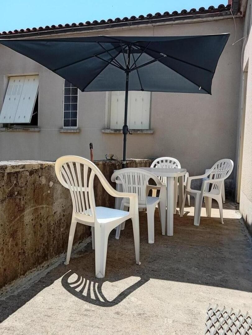 Een terras met een tafel, stoelen, een parasol en een muur met ramen.