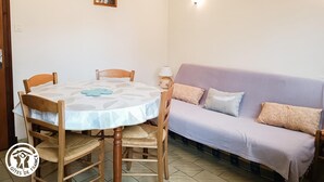 A dining area with a round table, four wooden chairs, a sofa, and a wall-mounted lamp.