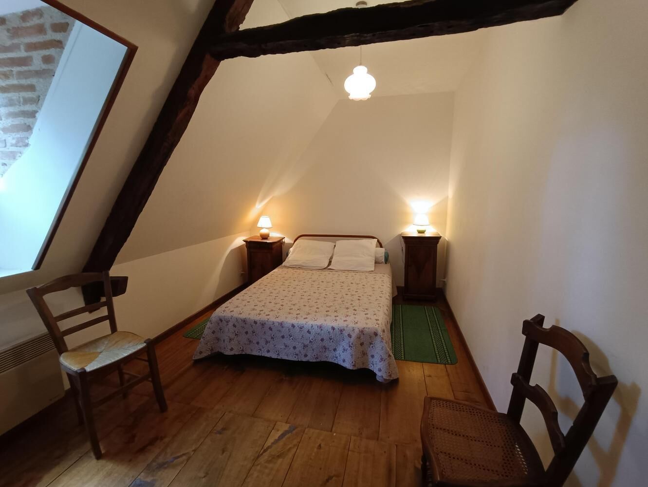 A cozy attic bedroom with a bed, two chairs, and a wooden floor.