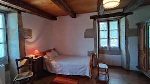 Ein gemütliches Schlafzimmer mit Holzbalkendecke, einem Einzelbett, einem Nachttisch, einem Sessel und einem Fenster mit Blick.