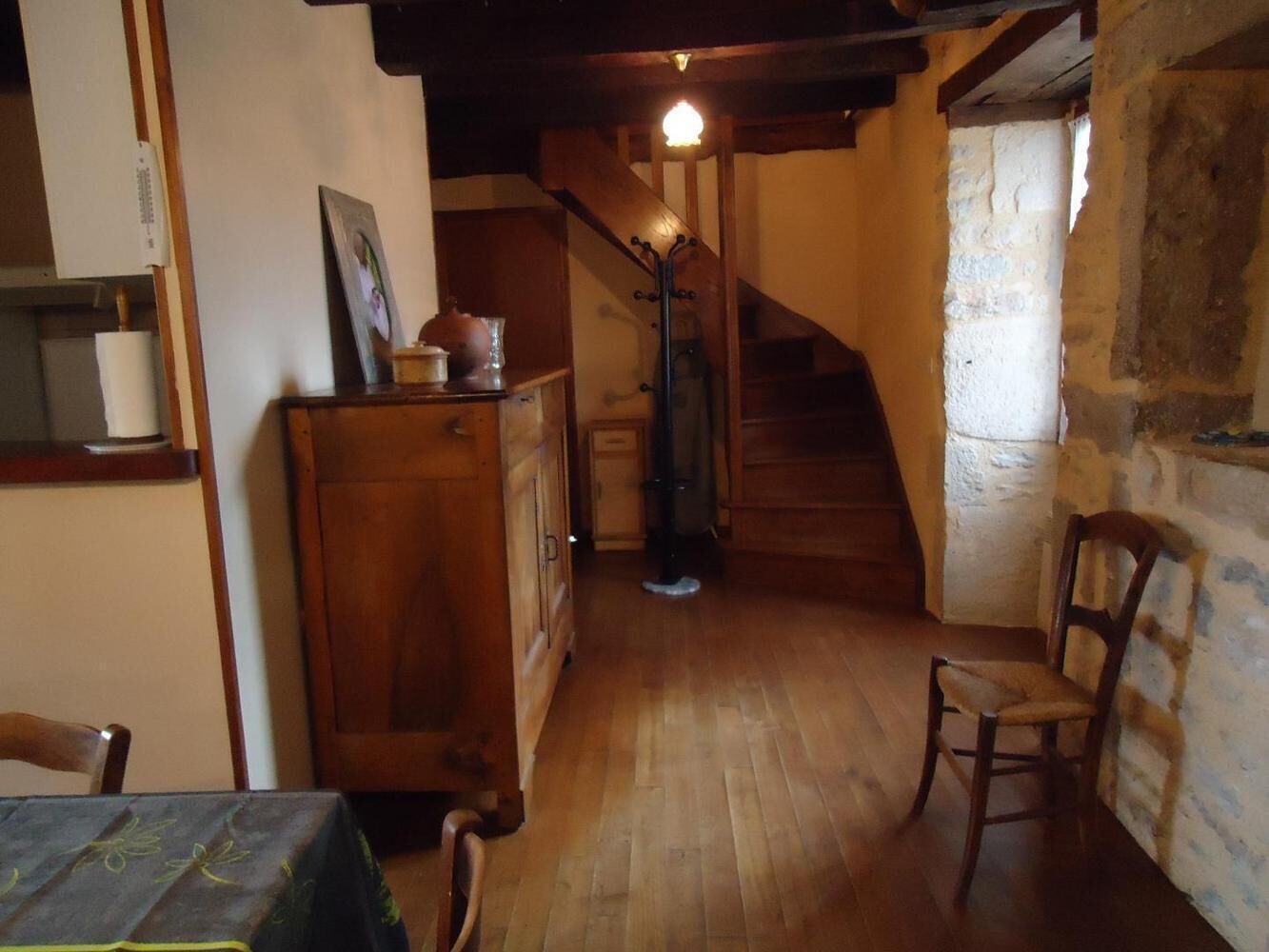 Ein rustikaler Innenraum mit einer Holztreppe, einem Esstisch mit Tischdecke und einem hölzernen Stuhl.