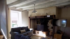 A living room with a sofa, TV, fireplace, and a wooden table. - Gîtes de France® - The Presbytery (SENAILLAC-LATRONQUIERE)