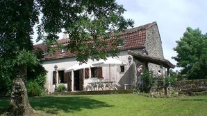A rustic house with a stone facade, a tiled roof, and a small porch with outdoor seating. - Gîtes de France® - LA TOURONDELLE (BEAUREGARD)