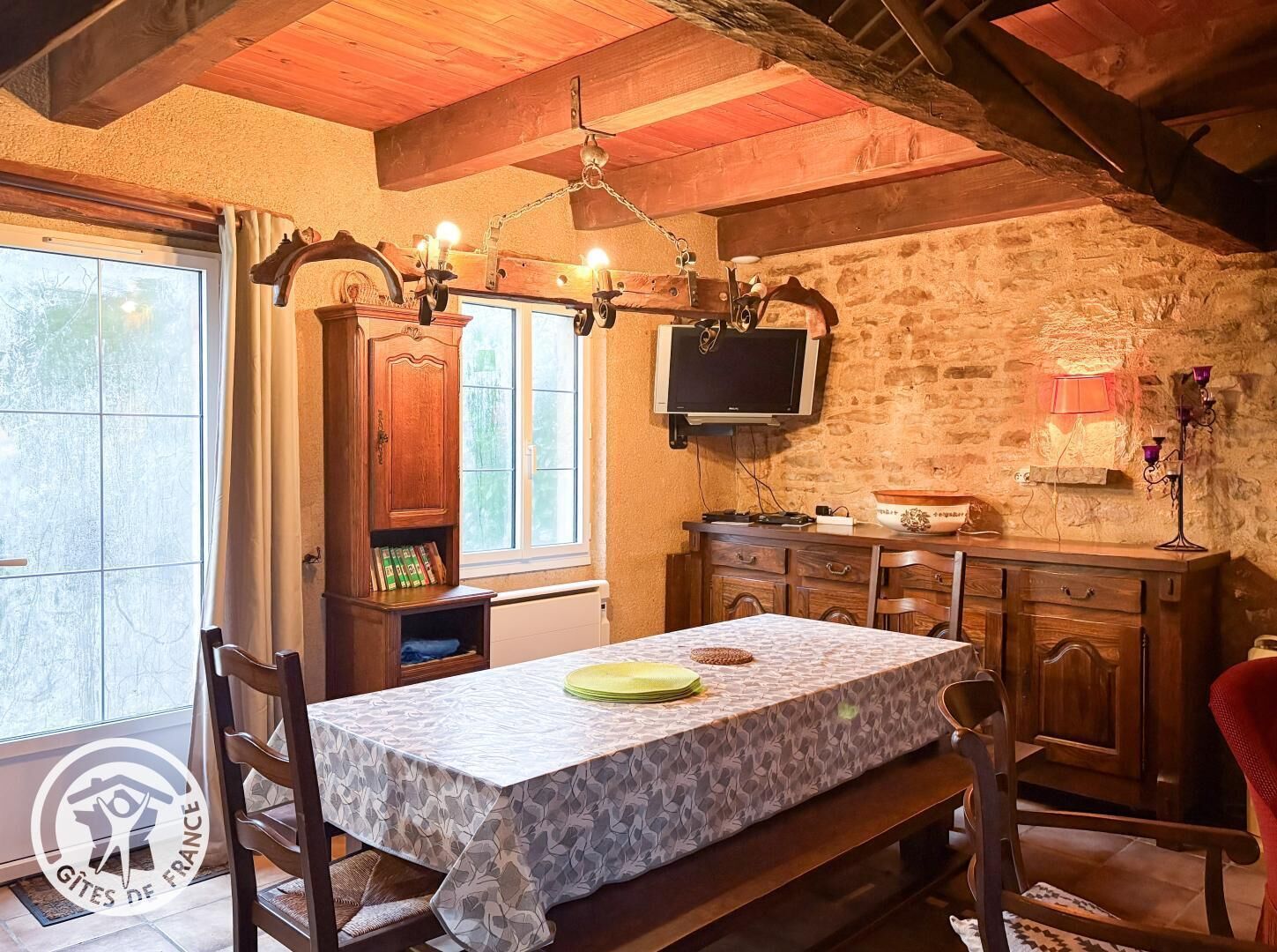 Un comedor acogedor con una mesa dispuesta para dos, un mueble de madera con un televisor encima y una pared de piedra al fondo.