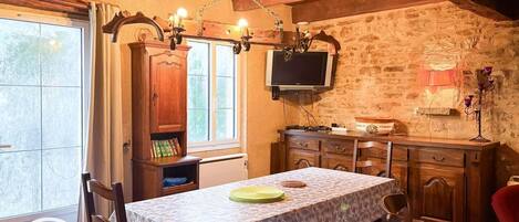 Un comedor acogedor con una mesa dispuesta para dos, un mueble de madera con un televisor encima y una pared de piedra al fondo.