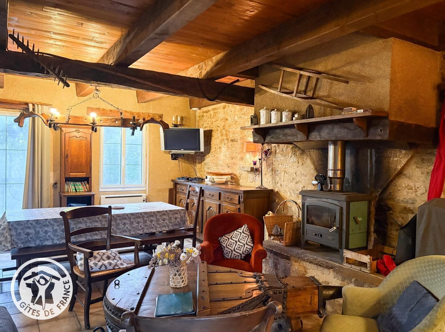 Ein rustikales Interieur mit einer Steinwand, Holzbalken, einem Kamin, einem Fernseher und einem Essbereich mit Tisch und Stühlen.