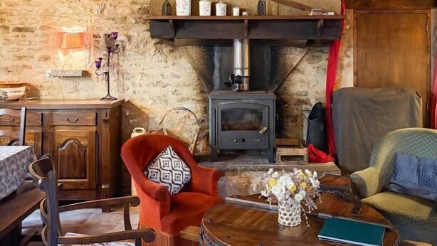 A rustic room with a stone wall, wooden furniture, a fireplace, and a small table with a vase. - Gîtes de France® - LA TOURONDELLE (BEAUREGARD)
