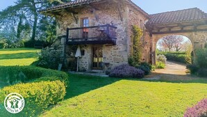 A stone house with a balcony, surrounded by well-maintained gardens and a clear sky.