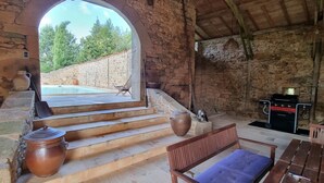 A rustic stone building with a pool, wooden benches, and a stone wall.