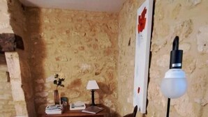 Una stanza con parete in pietra, una scrivania in legno con una lampada, una sedia e un letto.