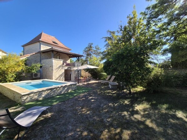A house with a swimming pool, outdoor seating, and a tree.