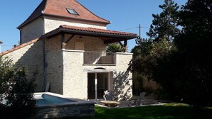 A two-story stone house with a red-tiled roof, a balcony, and a swimming pool. - Gîtes de France® - Le Pigeonnier des Junies (CAHORS)