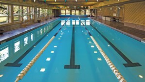 Une grande piscine intérieure avec des couloirs clairement délimités, des murs en bois et des plantes en pot disposées le long des bords.