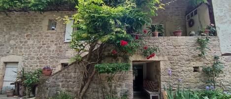 A rustic stone building with a small entrance, surrounded by lush greenery and potted plants.
