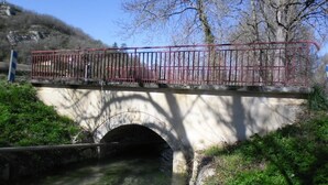 Un puente de piedra con barandilla de metal sobre un arroyo.