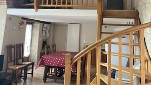 A wooden staircase leading to a loft bedroom with a sloped ceiling and a dining area below. - Gîtes de France® - GITE LAGINESTIERE (CREGOLS)