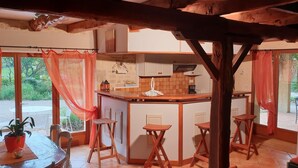 A rustic kitchen with a wooden bar, three stools, and a large window with curtains. - 46g11622 - Lherm - Gîte (LHERM)