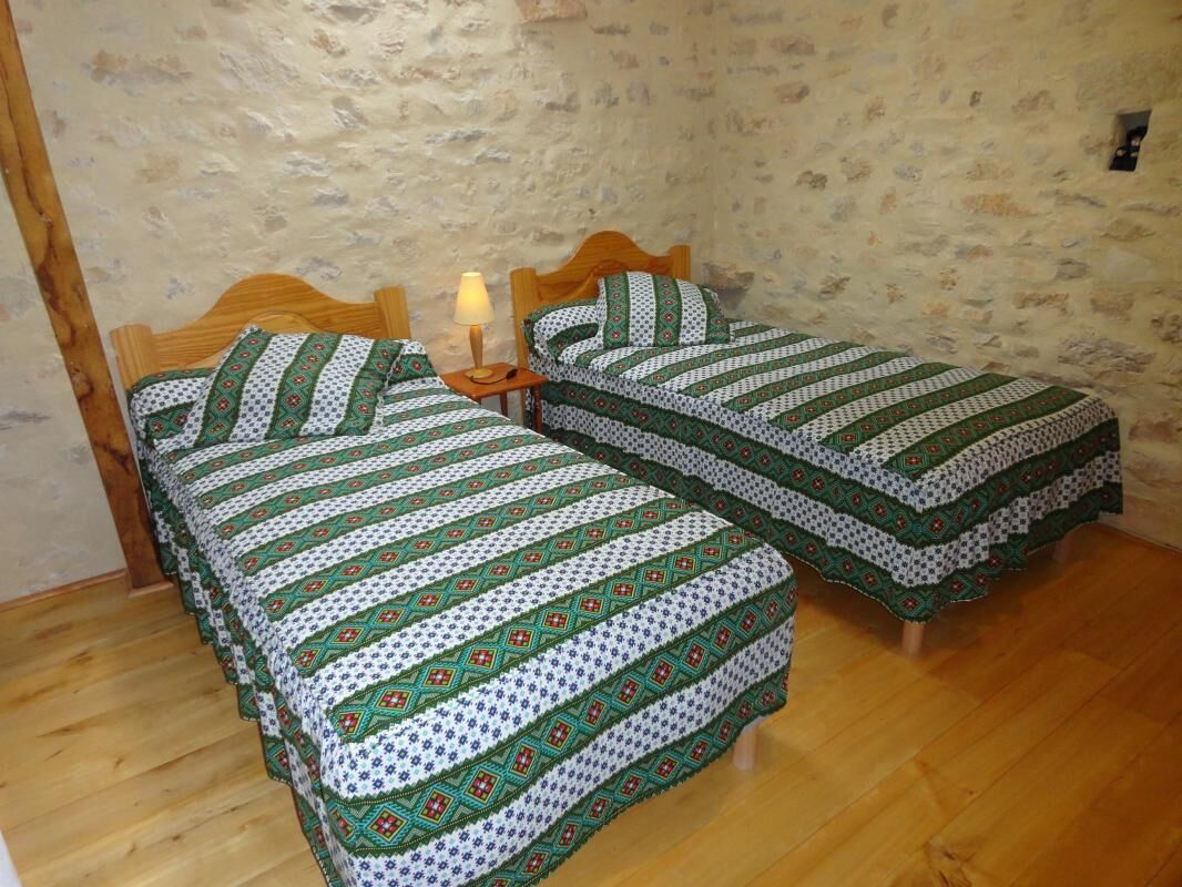 Een kamer met twee houten bedden, elk voorzien van een beddekleed met dessin en kussens.