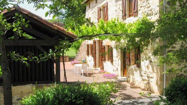 A stone building with wooden shutters, a covered patio, and outdoor seating. - Gîtes de France® - Lou Sécadou (CUZAC)