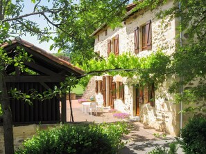 Un bâtiment en pierre avec des volets en bois, un patio couvert et des sièges à l’extérieur.