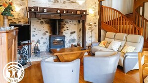 A cozy living room with a stone wall, a wooden staircase, and a fireplace. - Gîtes de France® - Lou Sécadou (CUZAC)