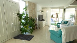 A modern living room with a teal sofa, a large potted plant, a small table, and a TV. - Gîtes de France® - LE PATIO DU BARRY (SAINT-VINCENT-RIVE-D'OLT)