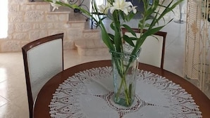 A dining area with a round table, chairs, and a vase of flowers. A staircase with ornate railings is visible in the background. - Gîtes de France® - LE PATIO DU BARRY (SAINT-VINCENT-RIVE-D'OLT)