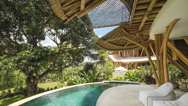 A pool area with a curved edge, surrounded by lush greenery and a bamboo structure overhead. - Ahura Luxury Villas (Pecatu)