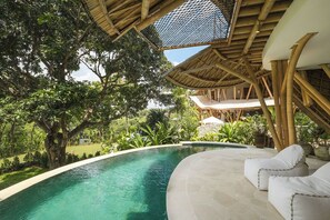 A pool area with a curved edge, surrounded by lush greenery and a bamboo structure overhead. - Ahura Luxury Villas (Pecatu)