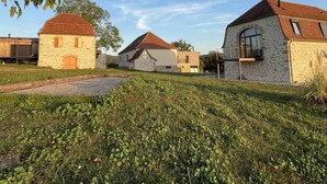 Une rangée de bâtiments en pierre aux toits rouges, entourés d’herbe verte et d’arbres.