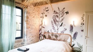Une chambre avec un mur en pierre, un lit avec du linge de lit blanc, une tête de lit en bois et des lampes fixées au mur.