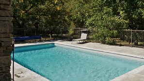 Una piscina rectangular con bordeado de azulejos, rodeada por una valla metálica y árboles.
