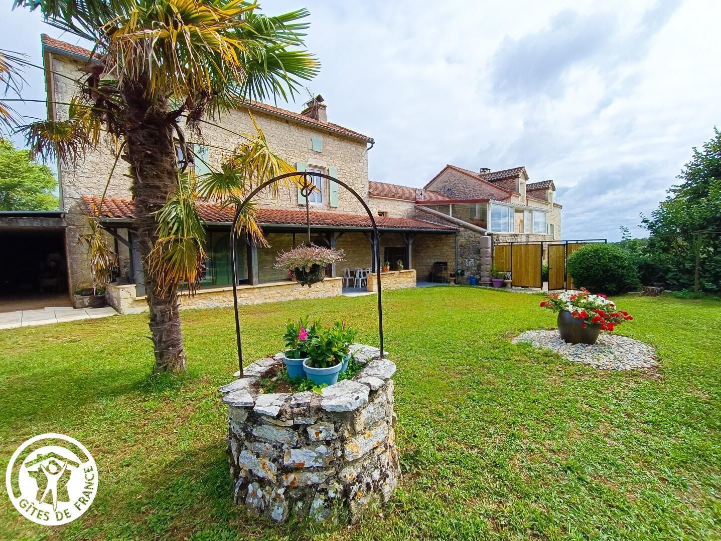 A stone house with a tiled roof, a covered patio, and a well-maintained lawn.