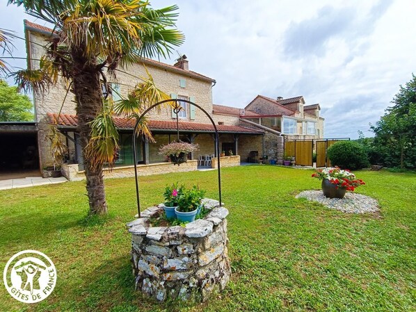 A stone house with a tiled roof, a covered patio, and a well-maintained lawn.