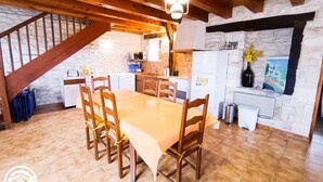 A rustic kitchen with a wooden table and chairs, a stone wall, and a hanging light fixture. - Gîtes de France® - La Bergerie (LALBENQUE)