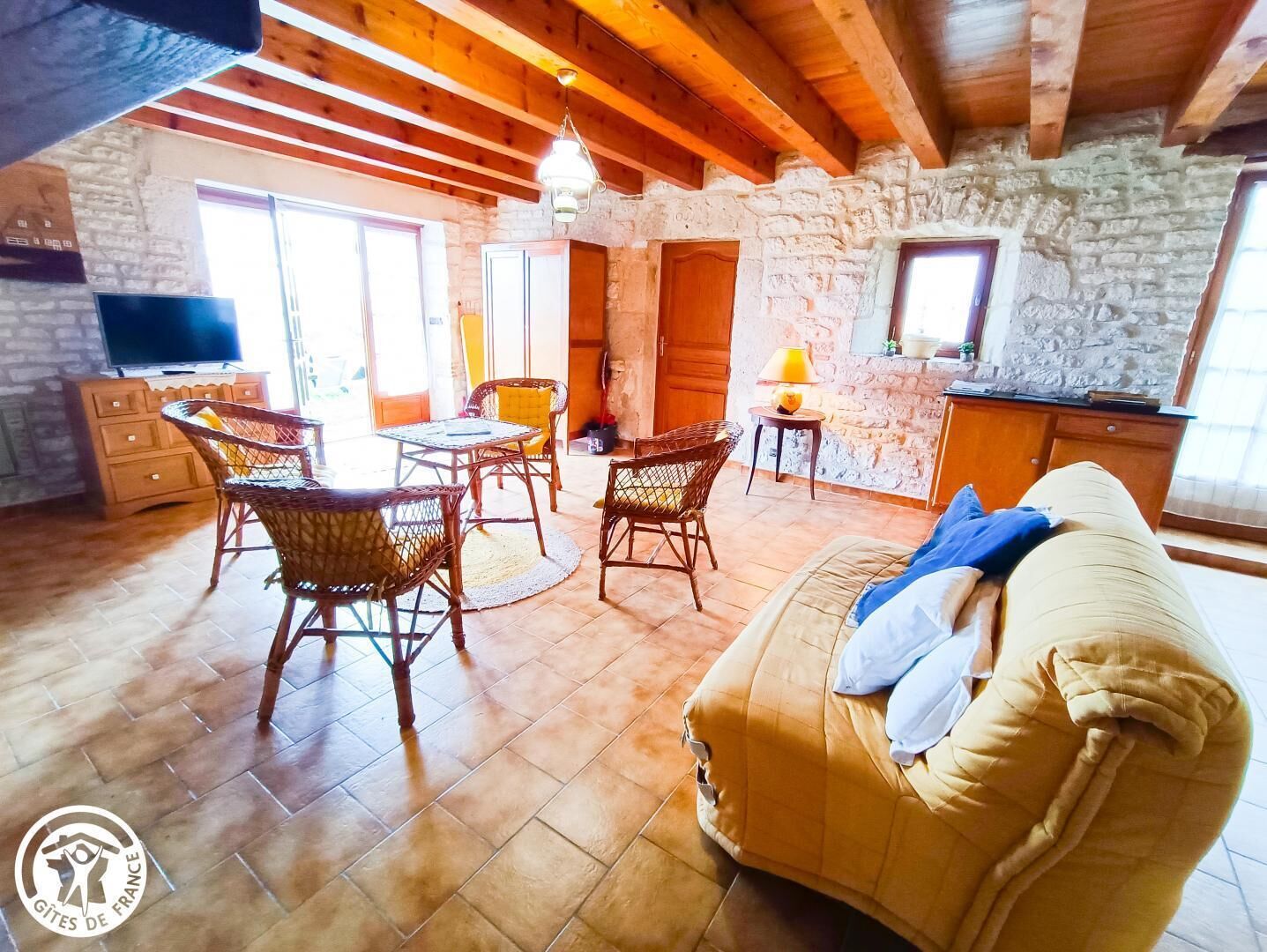 Una sala acogedora con un sofá, sillas de mimbre, una mesita y un televisor.