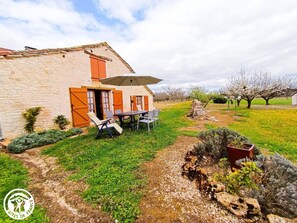 A stone house with a patio, outdoor seating, and a garden. - Gîtes de France® - La Bergerie (LALBENQUE)