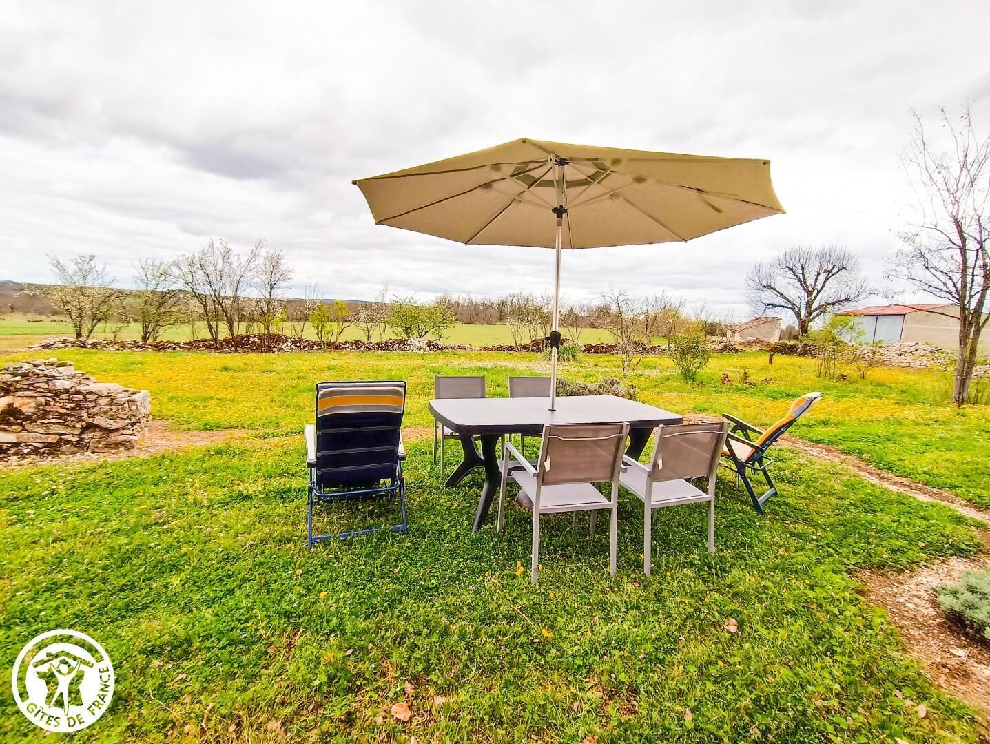 An outdoor dining area with a table and chairs, a large umbrella, and a stone wall in the background.