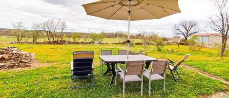 An outdoor dining area with a table and chairs, a large umbrella, and a stone wall in the background.