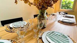 A dining table set with plates, cutlery, and wine glasses, surrounded by chairs, with a vase of dried flowers in the center. - Gîtes de France® - Le Loft Gramat (GRAMAT)