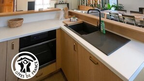 A modern kitchen with a central island, wooden cabinets, and a hanging pendant light. - Gîtes de France® - Le Loft Gramat (GRAMAT)