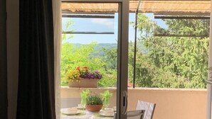 Un balcone con un tavolo apparecchiato per due, una pianta in vaso e vista su vegetazione e una struttura con tetto di paglia.