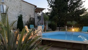 Una terrazza in legno con piscina, sedie a sdraio e un edificio in pietra sullo sfondo.