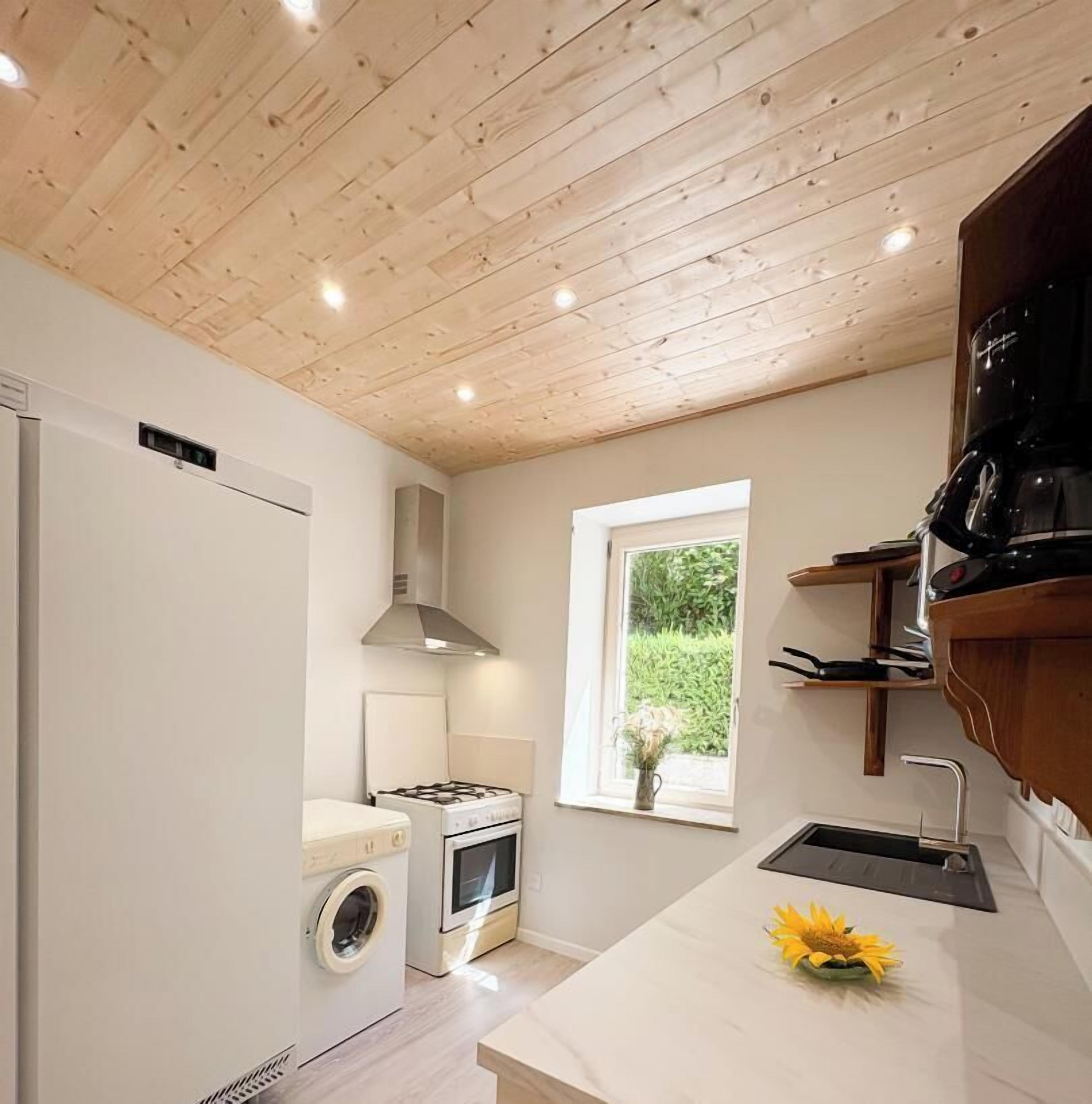 Cocina compacta con lavadora, horno y ventana con vista a follaje.