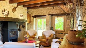 A cozy room with a fireplace, leather chairs, a wooden table, and a large window with a view of greenery.