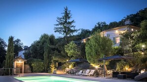 A swimming pool with lounge chairs and umbrellas, surrounded by trees and a stone building.