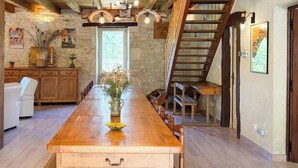 A wooden dining table with chairs, a vase with flowers, and a staircase leading to an upper level.