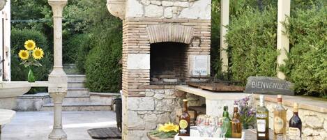 An outdoor patio with a stone-built oven, a welcome sign, and a table set with bottles and glasses.