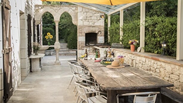 An outdoor patio with a stone archway, a wooden table, and a pizza oven.
